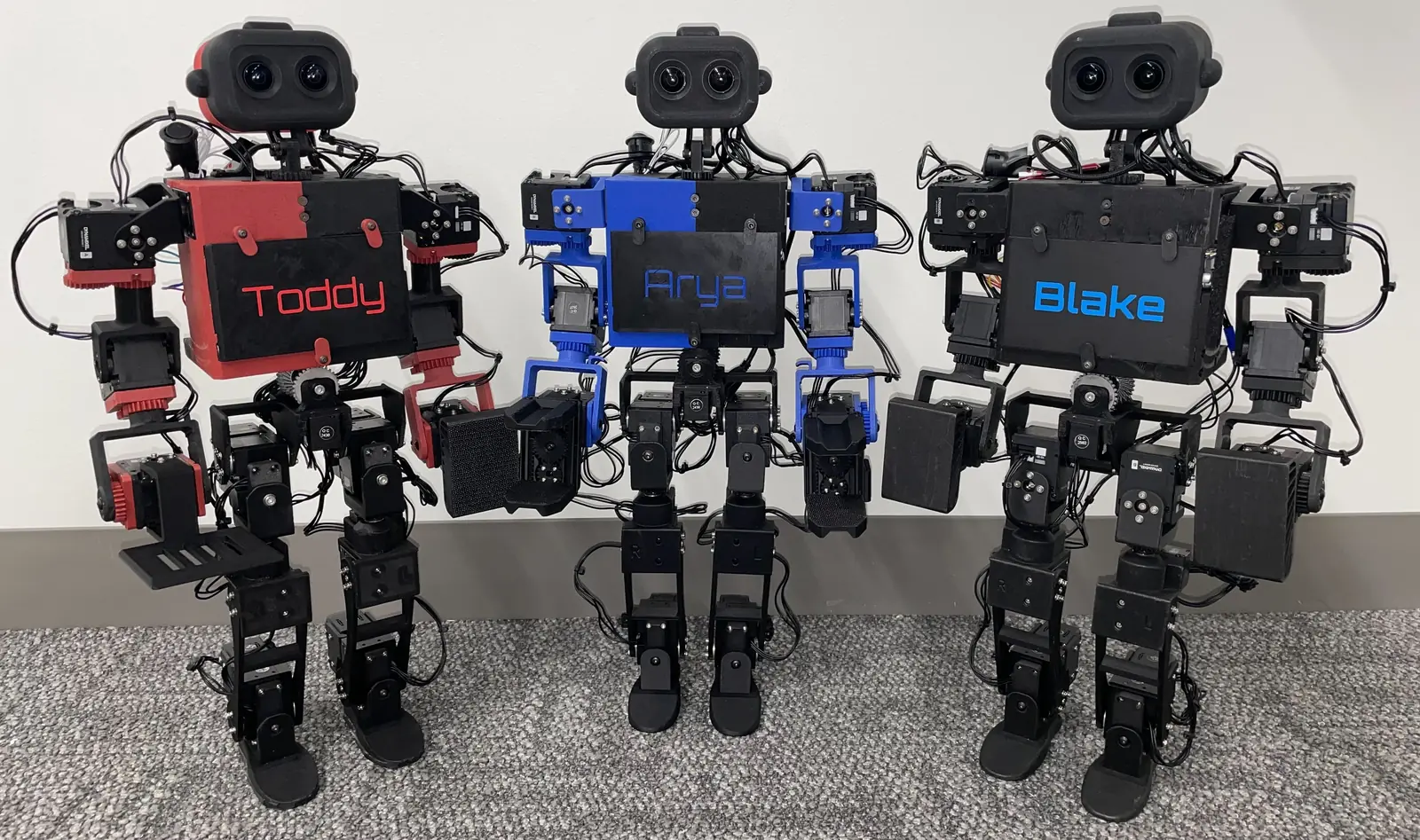 Three ToddlerBot humanoids standing side by side with coloured chest panels